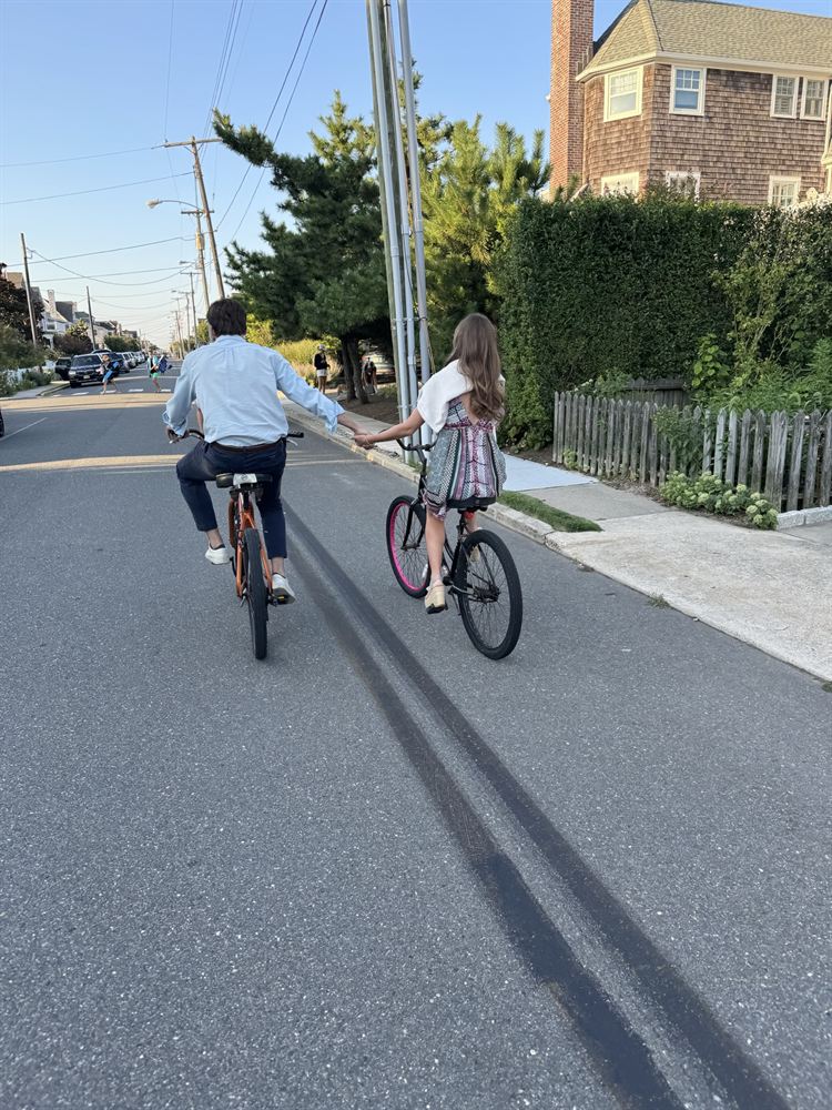 Riding bikes down a beach-town street, holding hands